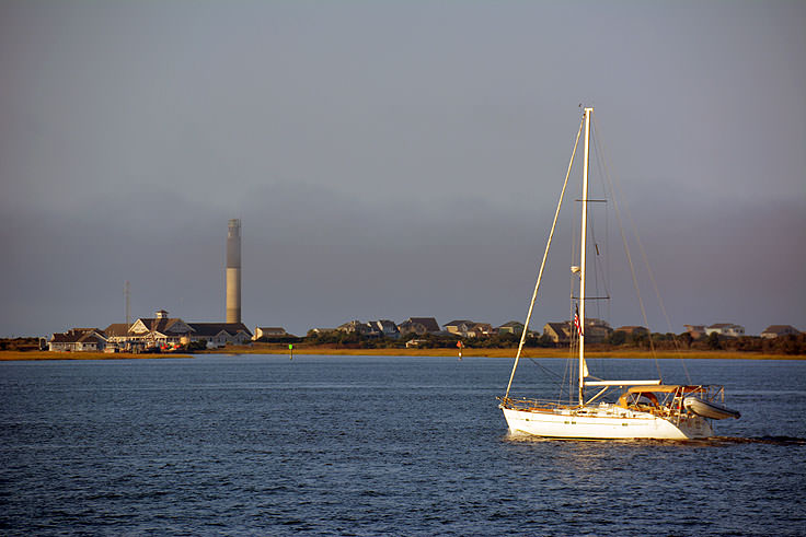 A sailboat in front of Oak Island lighthouse, from Southport NC